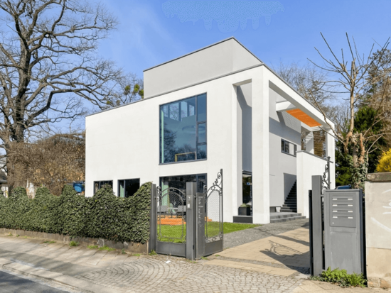 Ein modernes weißes Haus mit großen Fenstern, orangem Vordach und verziertem Metalltor an einem sonnigen Tag.