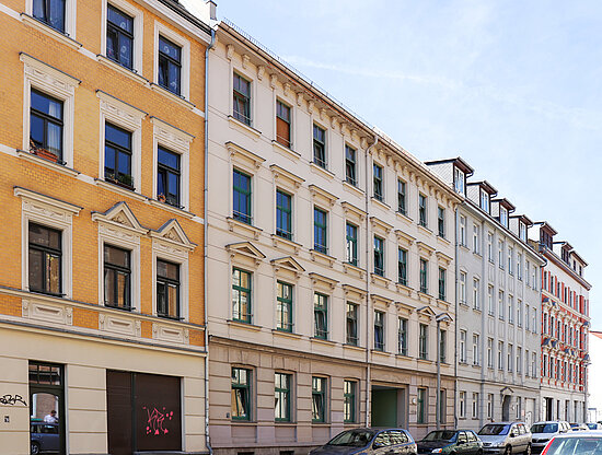 Seitenansicht einer Straße mit verschiedenen, mehrstöckigen Apartmentgebäuden in Gelb, Creme und Rot, mit parkenden Autos.