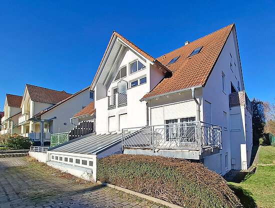Reihe weißer Häuser mit roten Ziegeldächern, Balkonen und gepflastertem Weg unter klarem blauem Himmel.