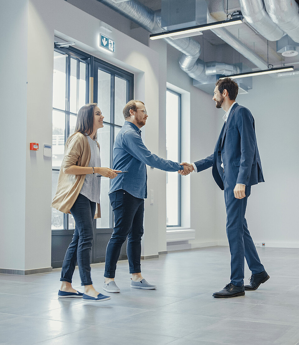 Drei Personen schütteln sich in einer leeren Gewerbeimmobilie die Hände, symbolisch für einen Geschäftsabschluss.