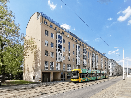 Modernes Wohnhaus mit geschwungenem Dach und Balkonen an einem sonnigen Tag. Eine gelb-grüne Straßenbahn fährt auf den Gleisen.