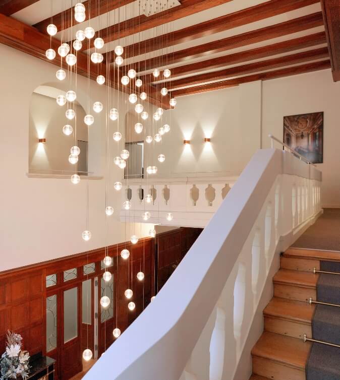 Luxuriöse Hotellobby oder Eingangsbereich mit großer Treppe und spektakulärem Kronleuchter aus vielen leuchtenden Kugeln.