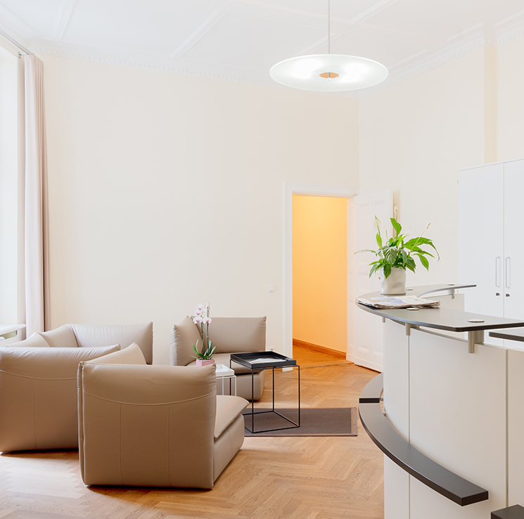 Heller, moderner Wartebereich mit beigen Sesseln, Parkettboden, weißem Empfang und Pflanze.